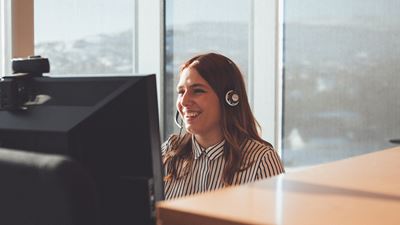 Kvinde med headset på kontor kigger ind i computer smiler