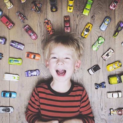 En dreng ligger på gulvet omgivet af legetøjsbiler og smiler stort