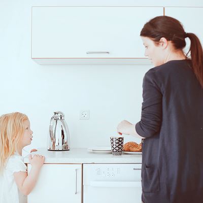 En mor står i køkkenet og taler med sin lille datter