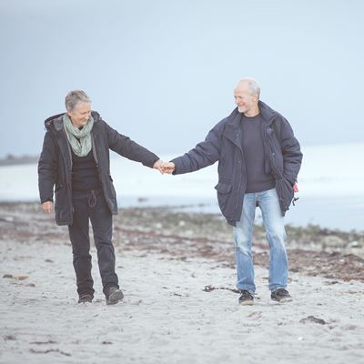 Et ældre par går tur på stranden hånd i hånd