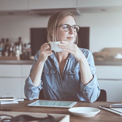 En kvinde som sidder ned ved sit bord derhjemme med en kaffe kop i hånden. 