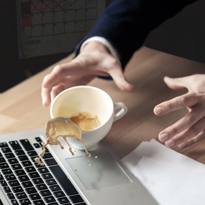 En mand er ved at spilde en kop kaffe i sin bærbare computer.