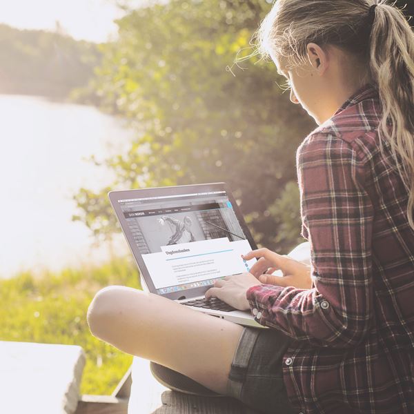 En ung kvinde sidder ved en sø og ser på BankNordiks hjemmeside på sin laptop