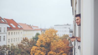 En ung mand læner sig ud af vinduet i sin lejlighed og ser på byen