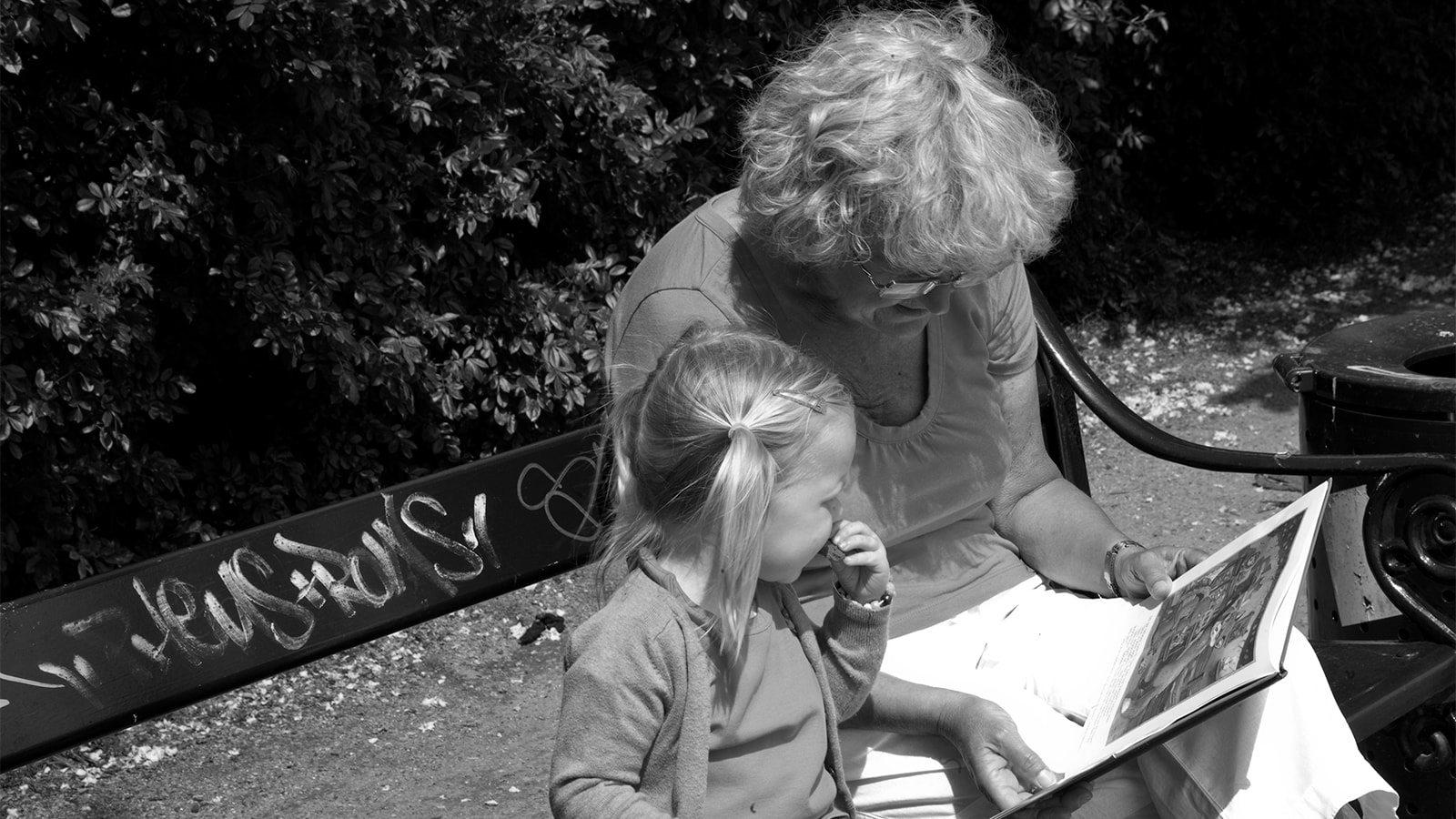 En bedstemor læser højt for sit barnebarn i en park