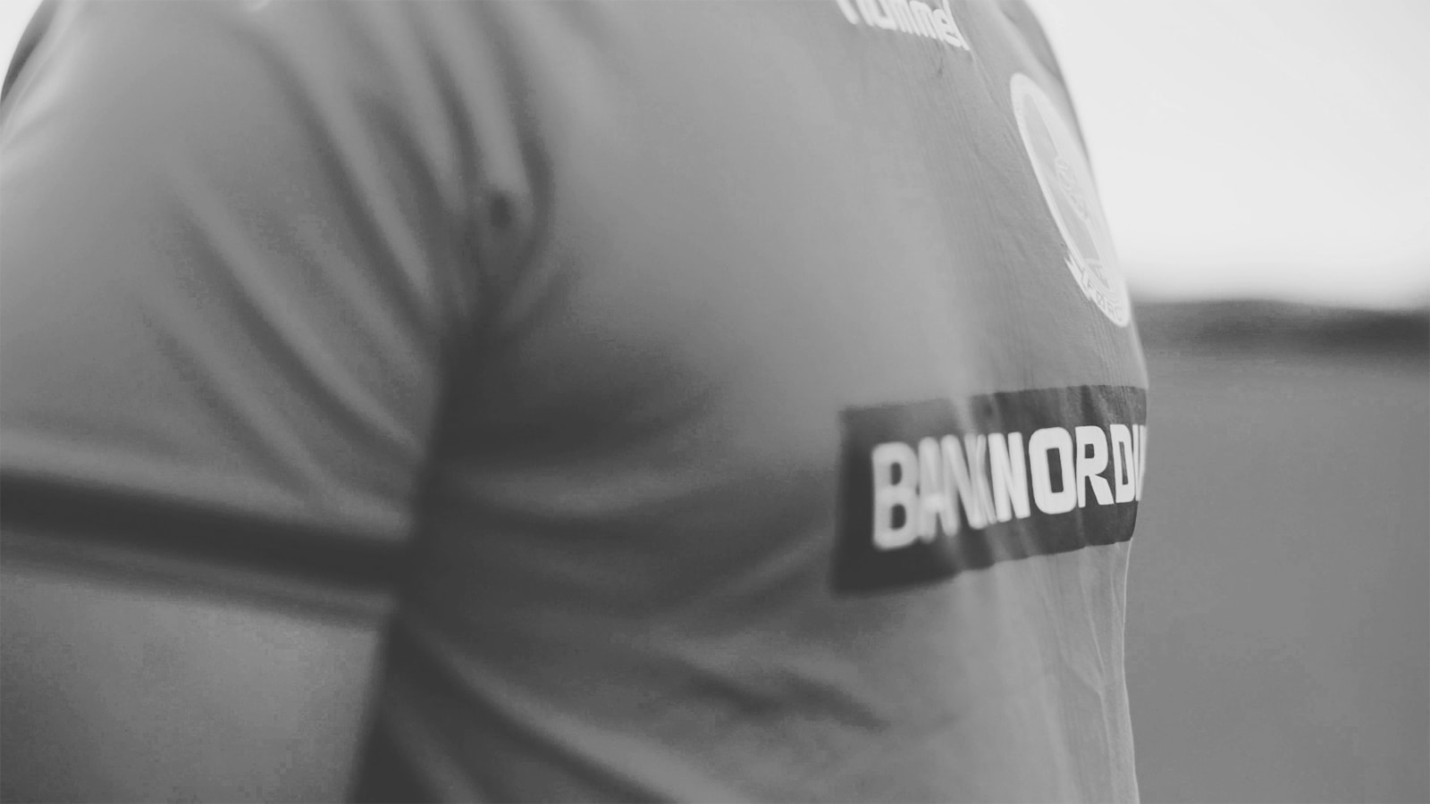 En fodboldspiller står på banen i sin trøje, der er sponsoreret af BankNordik