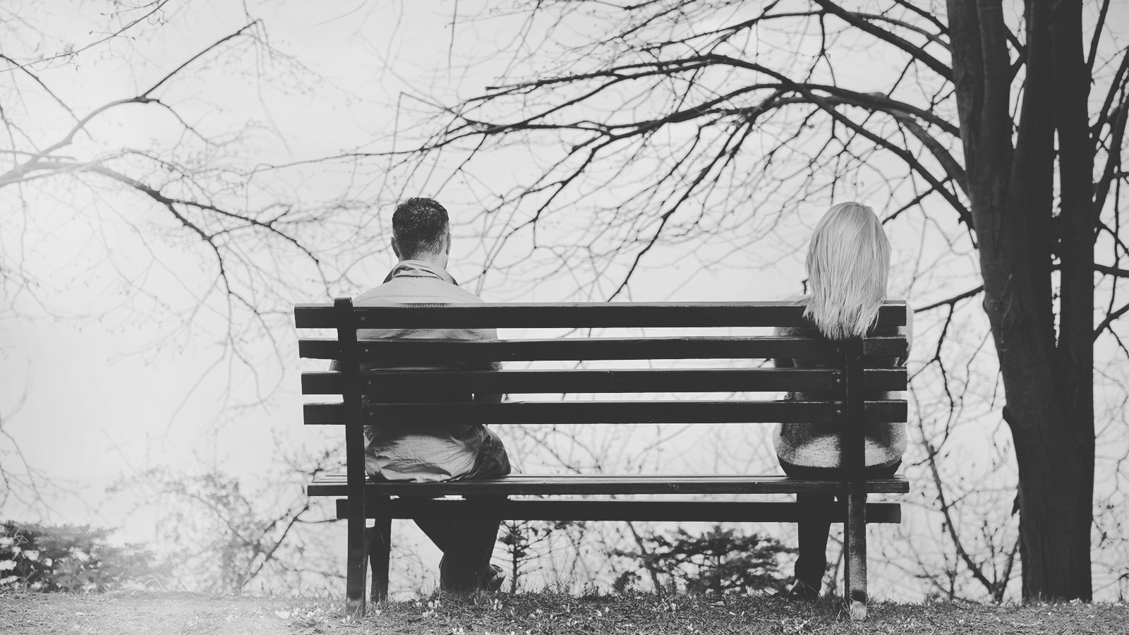 Et par sidder på en bænk med stor afstand mellem hinanden