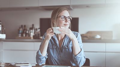 En kvinde som sidder ned ved sit bord derhjemme med en kaffe kop i hånden
