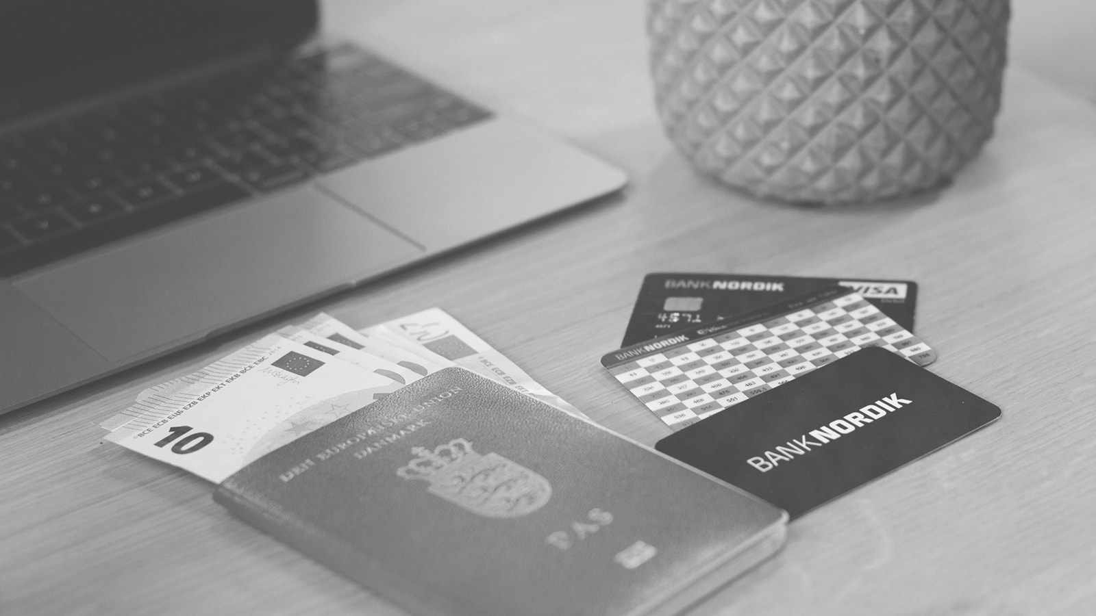 Et pas, betalingskort og eurokontanter ligger på et bord foran en computer. 
