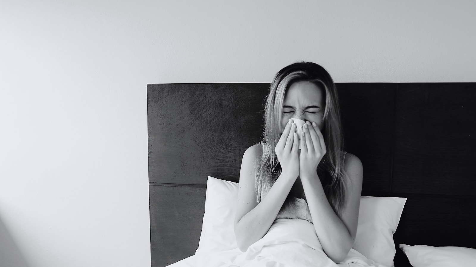 En kvinde nyser i sengen på sit hotelværelse.