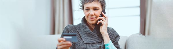 En dame kigger på sit betalingskort, mens hun taler i telefon.