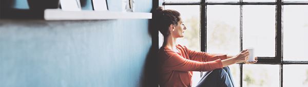 En kvinde sidder i en vindueskarm med en kop kaffe