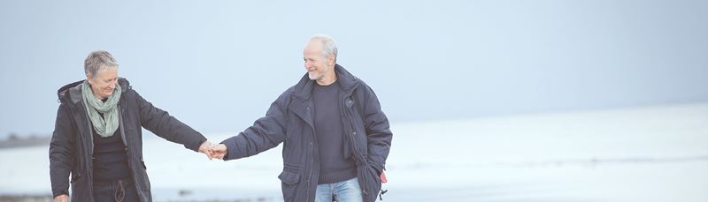 Et ældre par går tur på stranden hånd i hånd