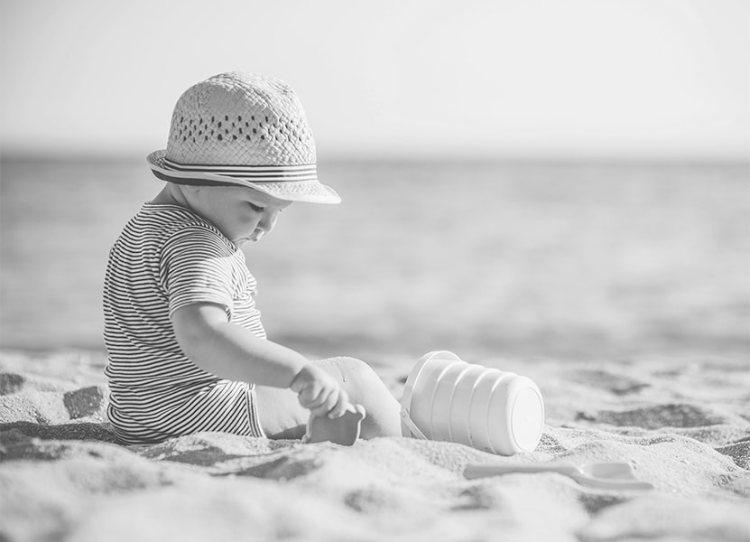 Et barn med solhat sidder på stranden og leger. 